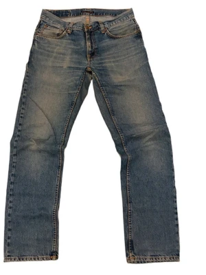 Blå raka jeans från Nudie Jeans - Säljer ett par klassiska blå jeans från Nudie Jeans med raka ben och snygga slitningar. Jeansen har fem fickor, orange sömmar och Nudie-loggan på bakfickan. Tillverkade i slitstark denim som ger en avslappnad look.