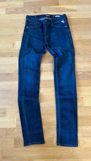 Replay jeans  - Säljer ett par mörkblå jeans från Replay med klassisk femficksmodell och raka ben. Jeansen har snygga kontrastsömmar, läderpatch bak i midjan och diskret Replay-logga på fickan. Tillverkade i slitstark denim som sitter skönt hela dagen.