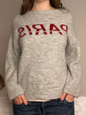 Grå stickad tröja med röd text🩶❤️ - Mysig grå stickad tröja med röd text framtill. Tröjan har en avslappnad passform, långa ärmar och ribbade muddar vid ärmslut och nederkant. Perfekt för dig som gillar enkel men trendig stil.🩶❤️