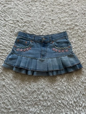 Jeanskjol med volang och broderi - En Lågmidjad ljusblå jeanskjol med broderade blommor omsydd från ett par jeans 🌺  Midjemått tvärsöver - 35cm, stretchig. Längd - 29cm