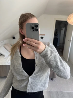 Ljusgrå mysig kofta med knappar - Ljusgrå kofta med rund hals och knäppning framtill. Koftan är stickad i ett mjukt material och har långa ärmar. 