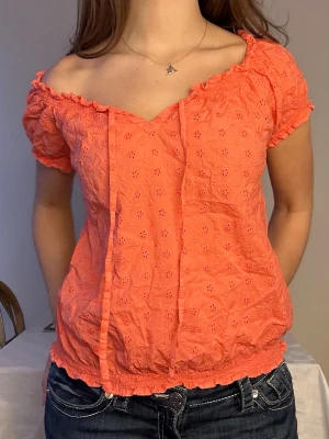 Korallfärgad blus med spetsdetaljer🧡 - Söt korallfärgad blus med korta puffärmar och broderade spetsdetaljer. Blusen har en omlottinspirerad v-ringning med knytband och elastiska kanter vid ärmslut och midja. Perfekt för vår och sommar!🧡