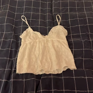 Vit spetslinnetopp med broderi - Söt vit linnetopp med tunna axelband och broderade blommor i spets. Toppen har en lätt v-ringad form och är luftig med ett romantiskt uttryck. Perfekt för varma dagar och kan stylas på många sätt.