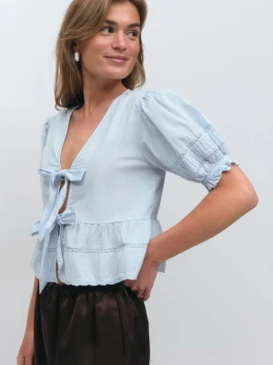 Ljusblå blus med puffärm och knyt - Supersöt ljusblå blus med puffärmar och två knyt framtill. Blusen har v-ringning, volang nedtill och fina spetsdetaljer på ärmar och midja. Tillverkad i ett lätt bomullstyg som känns luftigt och fräscht. Perfekt för en trendig och feminin look.