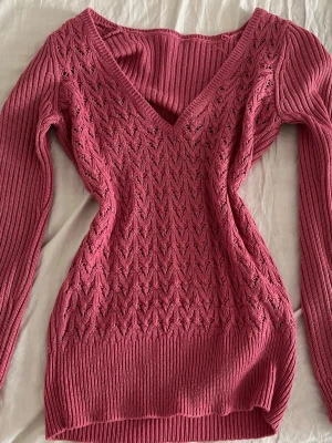 Rosa stickad tröja med V-ringning - Säljer en snygg rosa stickad tröja med V-ringning och långt ärm. Tröjan har ett detaljerat hålmönster framtill och ribbstickade muddar vid ärmslut och nederkant. Perfekt för dig som gillar en feminin och trendig look.