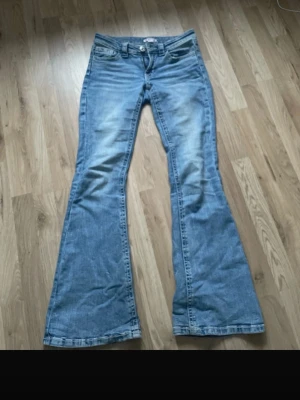Ljusblå bootcut jeans - Säljer ett par ljusblå bootcut jeans med låg midja och klassisk femficksdesign. Jeansen har en snygg tvättad look och vida ben som ger en retrovibe. Perfekta för dig som gillar 00-talsstilen och vill ha ett par jeans som sticker ut.