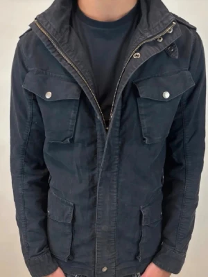 Fieldjacket Woolrich - Snygg mörkblå fieldjacket från Woolrich med fyra stora fickor framtill, dragkedja och knappar. Jackan har hög krage och en klassisk, snygg passform. Perfekt för dig som vill ha en stilren och funktionell jacka till vardags. Jag är runt 185 cm lång och väger runt 75 kg. Pris kan du diskuteras vid snabb affär! 