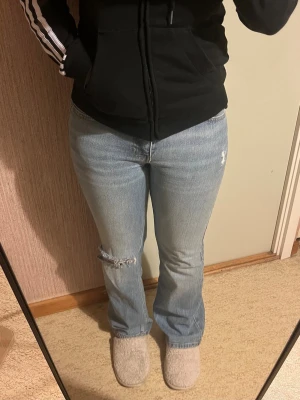 Ljusblå gina tricot bootcut jeans - Säljer ett par ljusblå jeans med bootcut passform och slitningar på ena benet. Jeansen har klassisk femficksdesign och är gjorda i denim med en skön, lite stretchig känsla. Har endast har använts en gång