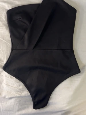 Svart asymmetrisk axelbandslös body - Snygg svart body från boohoo som är aldrig har använts. Sitter tight men materialet är också lite stretchigt. Storleken passar XS, men också XXS och S. Pris kan diskuteras och hör av er för fler bilder ❤️
