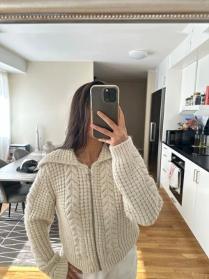 Vit stickad kofta kabelstickad - Säljer en chunky vit stickad kofta med bred krage och dragkedja framtill. Koftan har ett snyggt flätmönster och ribbade muddar vid ärmslut och nederkant. Perfekt för lager på lager och riktigt cozy vibes.