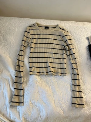 Randig ribbad långärmad topp - Trendig ribbad topp med långa ärmar i beige och svarta ränder. Croppad modell med rund halsringning, perfekt för en avslappnad och stilren look. Skön stretchig kvalitet.