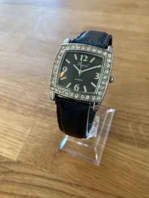 Regal R3740S 30mm Damur - Regal Quartz damklocka i nyskick (aldrig använd) med ett svart läderband. Klockan har en rektangulär boett med strassdetaljer runt urtavlan. Urtavlan är svart med silverfärgade siffror och visare. Baksidan av boetten är märkt med "WATER RESISTANT STAINLESS STEEL BACK R3740S". Behöver bara nytt batteri.  Nypris: 500 SEK Mitt pris: 189 SEK  Skickas alltid snabbt och spårbart. Skriv vid frågor och se gärna mina andra annonser!   GRATIS: För betalande kunder erbjuder jag personlig experthjälp för di