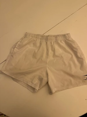Vita träningsshorts från Gymshark - Snygga vita shorts från Gymshark i storlek M. De har elastisk midja med snörning och är perfekta för träning. Tillverkade i ett lätt och bekvämt material som andas. Klassisk design med fickor på sidorna och diskret logga.