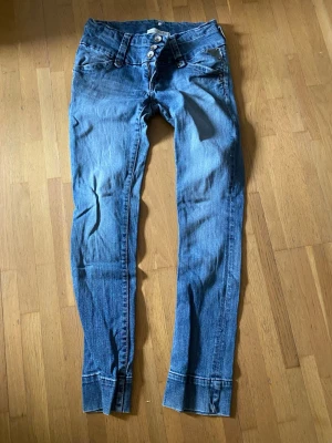 Stretchjeans  - Säljer ett par blå skinny jeans medflera knappar i gylfen. Jeansen har smala ben och slitningar för en cool look. Materialet är denim i bomull. 
