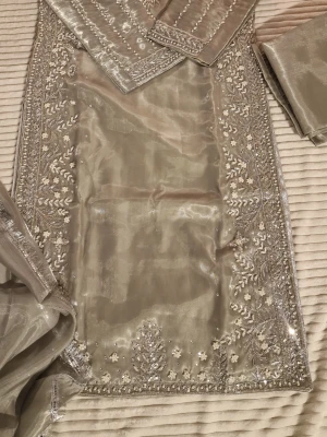Beige broderad långklänning - Elegant beige långklänning med detaljerad brodyr och pärlor längs kanterna. Klänningen har ett skimrande tyg och vackra broderade mönster som ger en exklusiv känsla. Perfekt för dig som vill sticka ut med en unik och stilren look.
