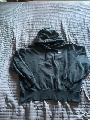 Svart hoodie från Nike med logga - Säljer en svart hoodie från Nike med den klassiska vita swoosh-loggan broderad på bröstet. Hoodien har huva med dragsko och ribbade muddar vid ärmar och nederkant. Perfekt för en avslappnad och sportig stil.