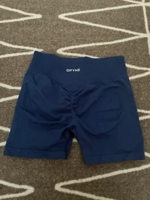 Blå träningstights shorts från DFYNE - Säljer Dfyne mörkblå sport/träningsshorts. Storlek S. Köpt från Vinted, så det finns ingen garanti för äkthet, men de verkar åtminstone högkvalitativa och innanför shortsen, som Dfyne, finns texten "Let nobody dfyne you". 🤍