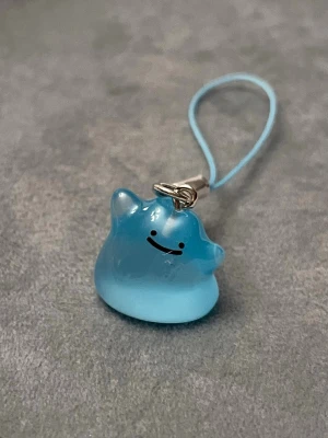 Shiny Ditto hänge berlock pokopia nyckelring Pokémon  - Jättegulligt hänge med en blå Ditto! Den är dessutom självlysande och lyser i mörkret.   OBS just denna berlocken har några repor på framsidan, därför säljer jag den till lägre pris.   Ditto-berlocken är ca 1,5 x 1,5 centimeter. Öglan är ca 5 cm lång.  Jättefin att sätta på din mobil, väskan eller i nycklarna exempelvis! Eller på ditt Switch eller DS