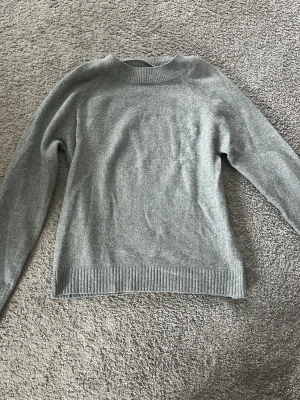 Grå stickad tröja från Vero Moda - Mysig grå stickad tröja från Vero Moda med rund halsringning och ribbade muddar vid ärmslut och nederkant. Enkel och stilren design som passar perfekt till jeans eller kjol. Tillverkad i mjukt material för extra komfort.