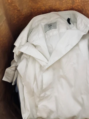 Vit skjorta från Michael Kors - Klassiska vit och blå skjortor från SIR, Michael Kors och Armani mfl med krage och knappar framtill. Skjortan är tillverkad i bomull och har en tidlös design som passar till många olika stilar. Perfekt för dig som gillar en clean och enkel look. Lägger även med två collegetröjor från WoodWood och Zara. Säljes som ett paket för 400:-