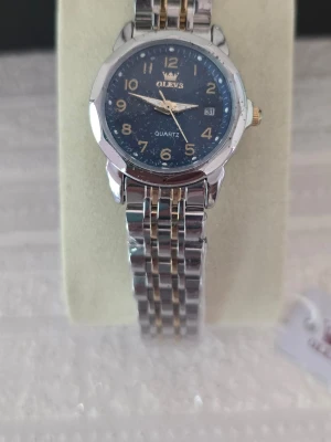 Silverfärgad klocka från Olevs rostfritt stål  - Stilren klocka från Olevs med blå urtavla och datumvisning. Armbandet är i silverfärgad metall med gulddetaljer. Klassisk rund form och tydliga siffror på urtavlan. Perfekt accessoar för dig som gillar en tidlös look.