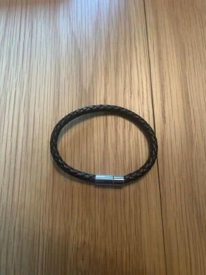 Brunt  flätat läderarmband - Stilrent brunt armband i flätat läder med ett magnetiskt spänne i silverfärgad metall. Perfekt accessoar för en enkel men snygg look. Passar både killar och tjejer som gillar minimalistisk stil.
