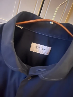 Mörkblå skjorta från Eton, slim fit - Snygg mörkblå skjorta från Eton i slim fit-modell. Klassisk design med knappar framtill och krage. Perfekt för dig som gillar stilrena plagg med hög kvalitet. Skjortan är tillverkad i bomull och har en tidlös look.