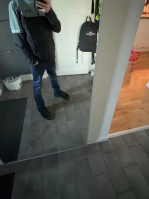 Svart och grå vindjacka från Under Armour - Säljer en svart och grå vindjacka från Under Armour med hög krage och dragkedja. Jackan har en sportig look och är perfekt för blåsiga dagar. Passformen är normal och jackan har långa ärmar. Snygg och enkel att matcha till olika outfits.