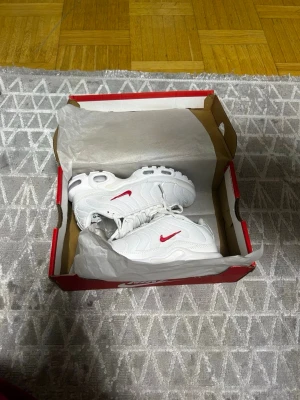 Nike Air Max Plus vita med röd swoosh - Säljer ett par Nike Air Max Plus sneakers i vitt med röd swoosh. Skorna har en chunky sula med synliga Air-enheter och detaljer i plast. Ovandelen är i mesh och syntetmaterial, och designen är sportig och modern.