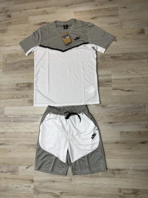 Nike shorts i vitt och grått - Nike shorts i vitt och ljusgrått med svart snörning i midjan och logga på vänster ben. Sportig design med kontrastpaneler och fickor på sidorna. Perfekta för träning eller chill dagar.