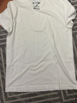 Vit t-shirt från Boss, storlek M - Klassisk vit t-shirt från Boss i storlek M. T-shirten har rund halsringning och korta ärmar. Tillverkad i mjukt bomullsmaterial för en skön känsla. Perfekt basplagg till garderoben.