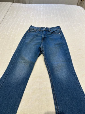 Blå raka jeans med hög midja - Säljer ett par klassiska blå jeans med raka ben och hög midja. Jeansen har fem fickor, gylf med knapp och dragkedja samt kontrastsömmar. Perfekta till en avslappnad stil och tillverkade i slitstark denim.