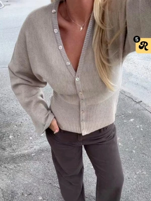 Beige ribbad kofta med knappar - Säljer en beige kofta med v-ringning och pärlemorknappar. Koftan har bred ribbad mudd i midjan och vid ärmsluten, samt en avslappnad passform. Köpt för 399kr och är nästan helt oanvänd .