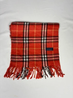Röd rutig halsduk från Burberrys - Snygg röd/orange halsduk från Burberrys i klassiskt rutigt mönster med inslag av svart, vitt, rosa och gult. Halsduken har fransar i ändarna och är tillverkad i mjuk ull. Perfekt accessoar för att lyfta din outfit med en ikonisk touch.