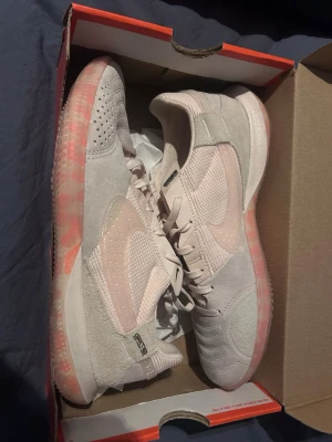 Nike vita och rosa sneakers - Säljer ett par snygga Nike sneakers i vitt och ljusrosa med mesh och mockadetaljer. Skorna har en genomskinlig sula med rosa mönster och klassisk Nike Swoosh på sidan. Perfekta för dig som gillar sportig och trendig stil.