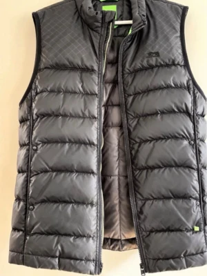 Svart dunväst från BOSS - Snygg svart dunväst från BOSS med en snygg och clean design. Dragkedjan är sönder men går säkert att fixa  (har inte orkat göra det). Den är använd därav priset.