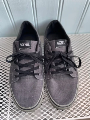 Vans Off The Wall Grå Canvas Strl 44 - Vans “Off The Wall” låga sneakers i grå canvas, storlek 44. Klassisk modell med svart snörning och vulkaniserad sula. Begagnade i gott skick med normala användningsspår. Sulorna visar slitage men bra mönster kvar. Se bilder för skick.