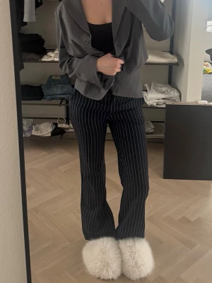 Svarta kostymbyxor med vita ränder - Snygga svarta kostymbyxor med vita vertikala pinstripes och raka ben. Byxorna har klassisk passform och är perfekta för en stilren look.