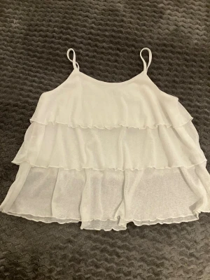 Vit volangig topp med tunna band storlek 146/152. - Supersöt vit topp med tunna axelband och flera lager volanger. Toppen är luftig och har en flowy passform, perfekt för varma dagar. Material polyester storlek 146/152 i mycket bra skick. 