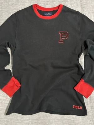 Polo Ralph Lauren Varsity Thermal Waffle Knit💋🔥 - Size L  Black waffle knit with red contrast trim Varsity “P” patch on chest + small POLO embroidery at hem  Y2K prep meets 2000s collegiate energy. Very 2007 private school but cool.  Perfect layered under a zip hoodie, denim jacket or worn fitted with cargos / low rise jeans.  From Polo sleepwear line but fully street wearable.  📏 Measurements: Shoulder to shoulder: 40 cm Pit to pit: 44–46 cm approx Length: 50 cm Sleeve: approx 58 cm.                                               Item#78