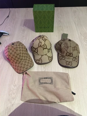 Beige keps från Gucci med GG-mönster - Säljer en beige keps från Gucci med klassiskt GG-monogram i brunt och grönt/rött band på sidan. Kepsen har böjd skärm och justerbar baksida. Tillverkad i canvasmaterial och levereras med originalpåse och låda.