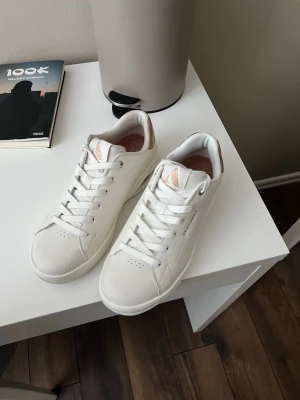 Vita Skechers sneakers i läder - Stilrena vita sneakers från Skechers i läder med klassisk låg profil. Skorna har vita snören, diskreta perforeringar vid tårna och detaljer i ljusrosa på plösen. Perfekta för dig som gillar en clean och enkel look.