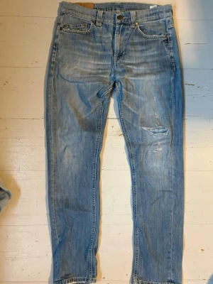 Dondup Jeans - Säljer ett par ljusblå jeans med raka ben och slitningar på framsidan. Jeansen har klassisk femficksdesign, knappgylf och detaljerade bakfickor. Perfekta för en avslappnad och trendig look. Dem är igentligen storlek 34 men sitter som 30.