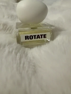 Parfym ROTATE med unik design - Parfym från caia med en fyrkantig, transparent glasflaska och en vit, äggformad kork. Flaskan har en modern och stilren look med tydlig etikett framtill. Den är limited edition och slutsåld. Nypris 695kr 