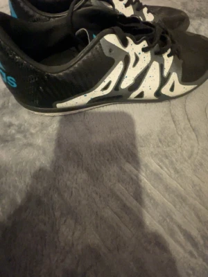 Adidas svartvita fotbollsskor - Säljer ett par Adidas fotbollsskor i svart och vitt med blå detaljer. Skorna har ett mönstrat syntetmaterial och snörning för bra passform. Perfekta för dig som vill ha stilrena och funktionella skor på planen.