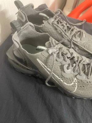 Nike grå sneakers med reflexdetaljer - Säljer ett par grå Nike sneakers med coola reflexdetaljer och sportig design. Skorna har mesh-överdel för bra andningsförmåga, synlig Air Max-sula och snörning. Perfekta för dig som gillar streetwear och vill sticka ut med stilrena detaljer.