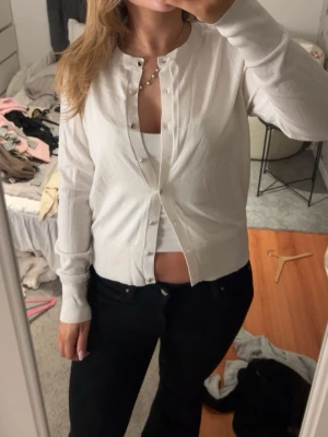 Vit klassisk kofta med pärlknappar - Snygg vit kofta med rund halsringning och pärlknappar framtill. Långärmad och i mjukt, tunt material som passar perfekt till lager-på-lager. Enkel och stilren design som funkar till många outfits.