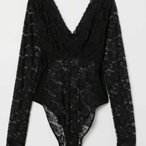 Svart spetsbody med lång ärm - Säljer en svart body i spets med v-ringning. Bodyn har långa ärmar och fina spetsdetaljer längs kanterna. Perfekt för att skapa en snygg lager-på-lager-look eller som statement-plagg. Strl 32/XXS. Köpt från H&M