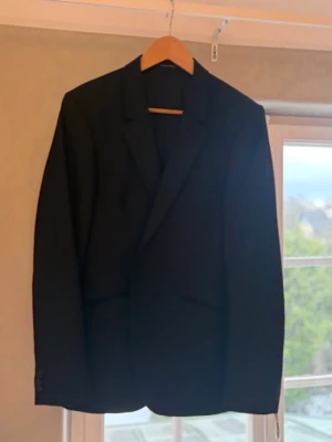 Svart kavaj från Tiger of Sweden - Klassisk svart kostym från Tiger of Sweden med smal passform och snygga slag. Tillverkad i ett slätt material som ger en stilren look. Superbra skick använd en gång.