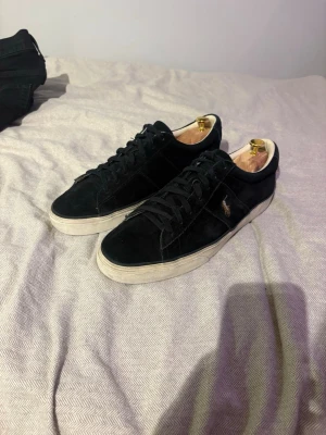 Mörkblå Polo Ralph Lauren suede sneakers storlek 44 - Snygga mörkblå sneakers från Polo Ralph Lauren i mocka med vit sula och diskret logga på sidan. Klassisk låg modell med mörkblå skosnören och bekväm innersula. Perfekta för en stilren och avslappnad look.
